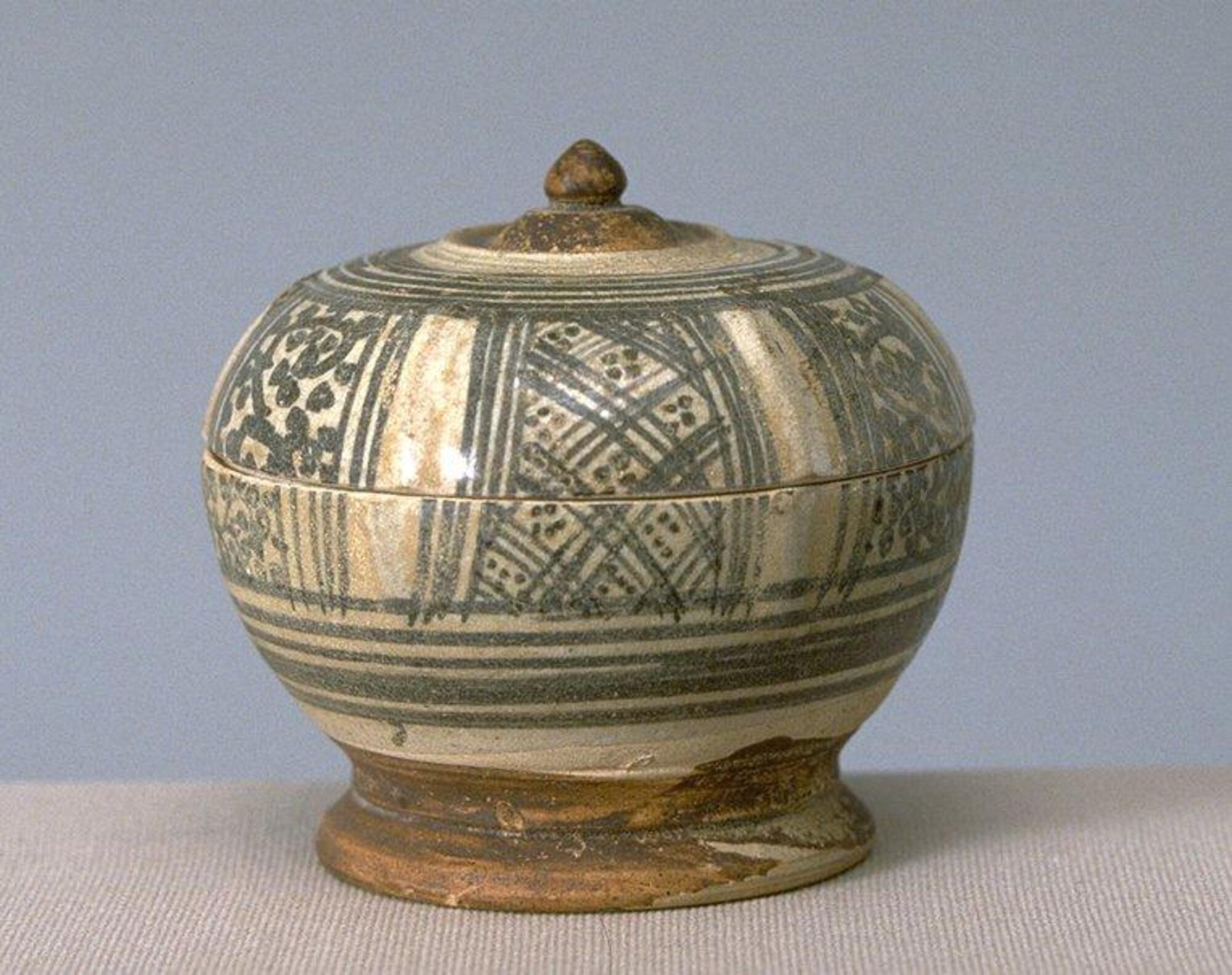 Small-size covered box, the lotus bud handle and surrounding medallion in brown, the body and lid with alternating panels of vegetal scrolls and lattices. Each panel is separated by a raised line. The foot is painted brown. Clear glaze.