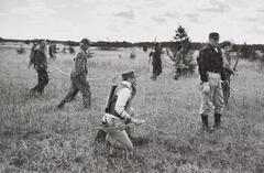 A photograph of twelve men in a field, wearing hunting gear and holding bows and arrows. In the foreground, a man kneels on the ground while everyone else stands.