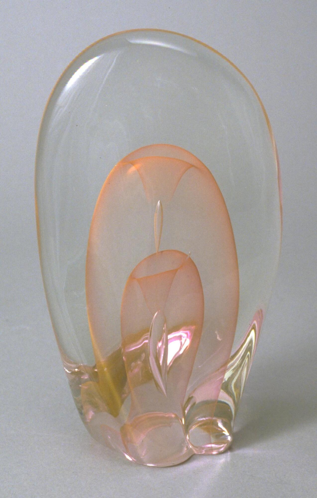 This glass sculpture is a large oval encasing a smaller pale peach oval which encases another smaller, darker peach oval like bubbles within bubbles. 