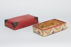 One box with a lid completely encompassing it. The lid has a red and black exterior and an interior with a geometric design in orange and blue hues. The box has the same geometric design on interior and exterior.