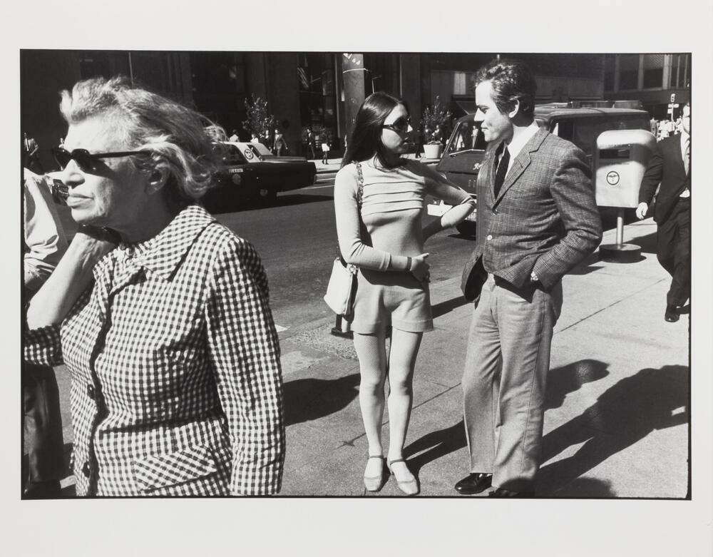 Photograph of a young man and woman stopped in the middle of the sidewalk to talk.