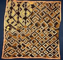 Square panel with  hemmed edges divided into four sections. The upper left section consists of opposing chevrons, while the lower left section consist of "x" styled patterns. The upper right section consist of diamonds formed by lines folding onto themselves while the lower right section consists of a grid of light tan diamond patterns. 