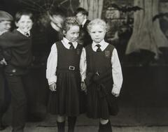 Two kids in uniforms standing in front of a large group of children.