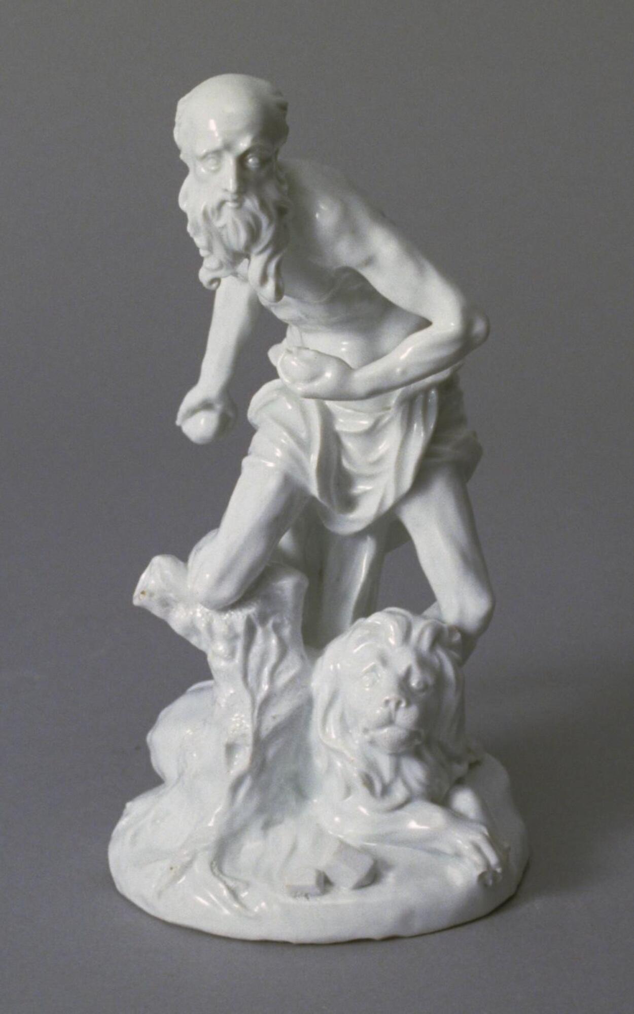 This small porcelain sculpture represents a gaunt, sinewy bearded figure, who is naked except for a loincloth. With his right knee wedged in a stump, his torso contracts with an inner tension as he pounds his chest with stones in an act of penitence. At his feet sits a lion.