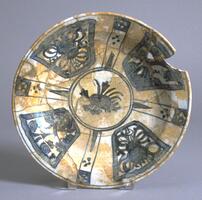 "Produced in the Wan Li era (1573-1619), the Chinese prototypes are more tightly controlled and more elaborate that the museum's Persian version. In place of nine rim panels in the Far Eastern piece our bowl has four, more widely dispersed over the rim area and enclosing loosely executed foliate forms. The elaborate scene usually appearing in the center of such bowls here is reduced to a simple bouqet, now in part reconstruction." 