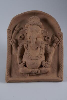 A relief of the elephant god, Ganesh. He has the head of an elephant with the body of a man. He is seated inside of an arch.