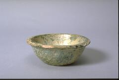 A flat bottomed, red earthenware bowl with rounded sides and everted rolled rim.  It is covered in green lead glaze, with iridescence and calcification. 
