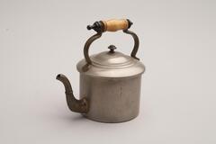 A pewter inkwell in the shape of a teapot. The handle is made out of wood and the spout is porcelain.