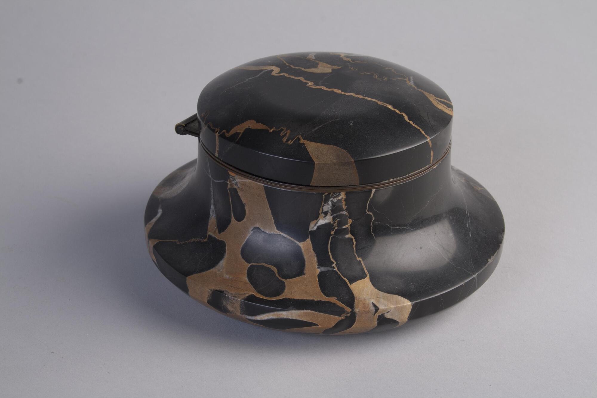 Inkwell made of black color marble has a flat and round body. There are some patterns on the marble that also serve as decoration on the body of the inkwell.