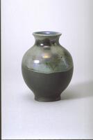 The lower half of this vessel has a matte black body; the upper half of the work is glazed with an iridescent pale blue.