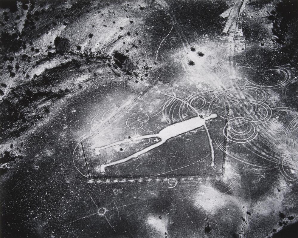 This photograph depicts an aerial view of an earth work of a human figure encased by the shape of a pentagon.