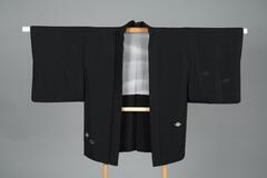 <p>Black formal chirimen haori with grey and silver black diamond motifs patched on the left front and right back sleeves and on the lower back and front with a gray inner lining. It has one family crest on the center on back.</p>
