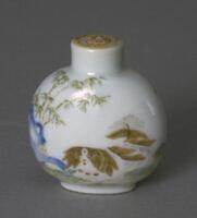 A globular white porcelain snuff bottle with a design of a Pekingese dog and bamboo.