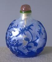 A clear circular glass snuff bottle with blue glass decorations on top depicting flowers and grasshoppers. On top is a green glass collar and rose quartz stopper.