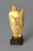 An ivory snuff bottle in the shape of seashell and fish. Carved on the body of the seashell are the scales and eyes of the fish. The bottom of the seashell curves and extends the up the side of the shell body in the shape of a tail. The top of the shell (where the mouth of the fish would be) is the stopper in the shape of a spiral shell. The snuff bottle is an incised wooden stand.