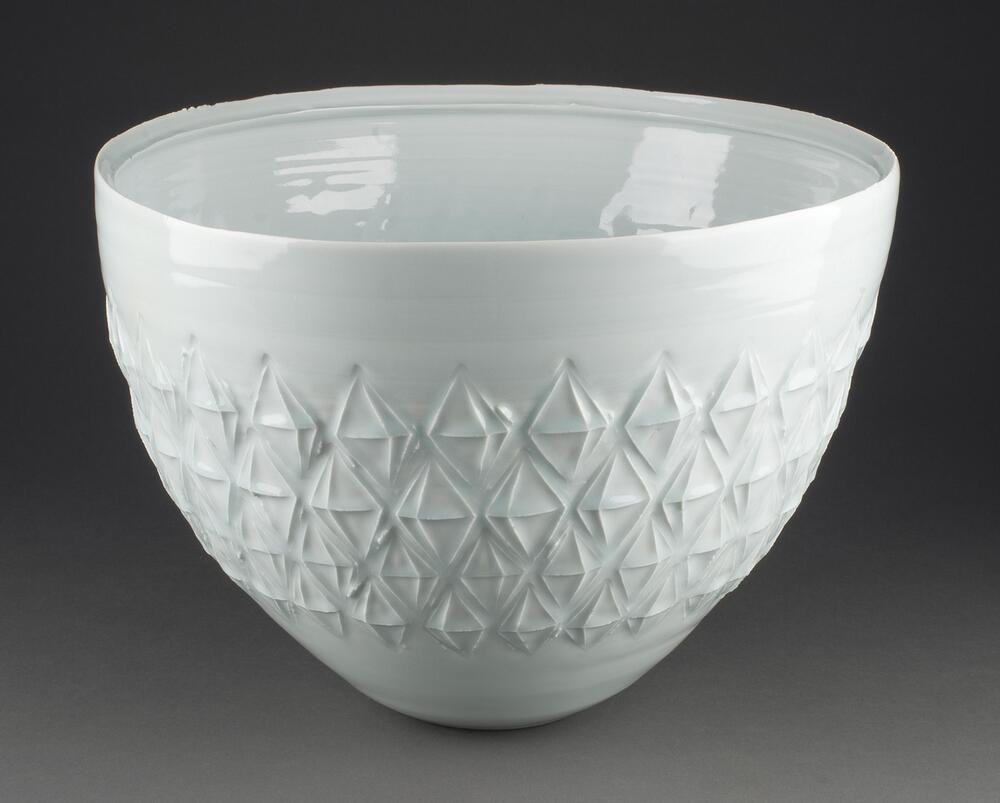 The large white bowl is round with a wide rim and a narrow bottom; almost like an up-side-down cone shape. Diamond patterns are stamped around the middle of the body. It has no foot. The rim is slightly warped.