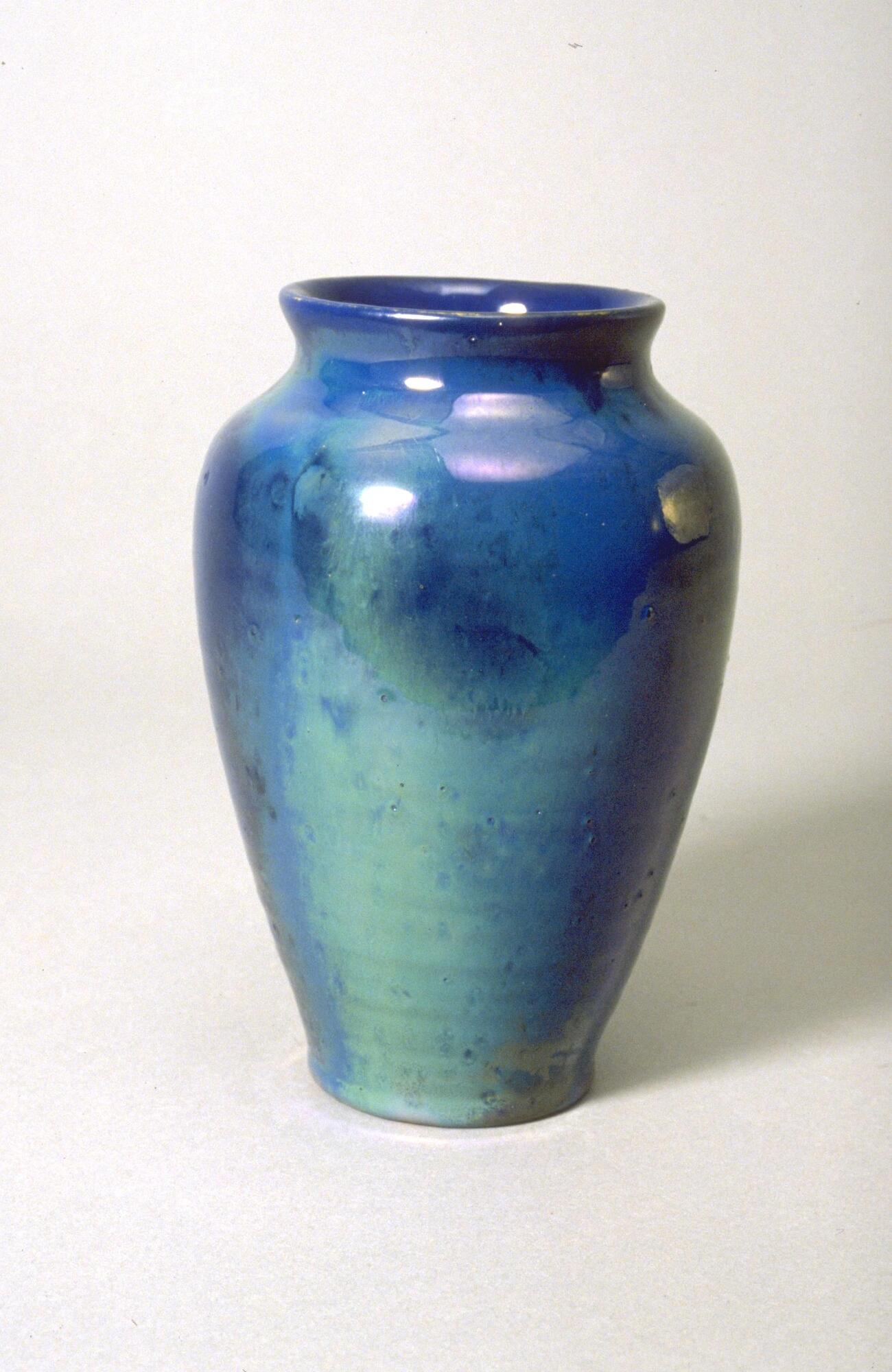 Ceramic vessel with rounded shoulder and wide mouth covered with an iridescent glaze over a semi-matte glaze that creates an appearance of irregular patches of color in shades of blue.  The rings of the thrown clay can be seen beneath the glaze.<br />