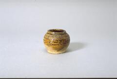 A thickly potted stoneware globular jar on a wide footring and wide mouth, with a direct rim on a straight short neck.  There  is a vertical wavy band of "S's" around the shoulder, and the interior and half the exterior is covered in a translucent brown glaze.  