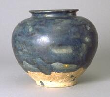 A buff stoneware globular jar, with a tapered base and wide, high shoulders, tapering to a wide, short neck with an everted rim. The work is covered in a mottled cobalt blue glaze. 