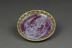 A purple and light blue spotted saucer with a gold metal rim.