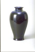 This vase has an elegantly tapering body based on Asian sources and has a dark iridescent glaze of black and blue hues.