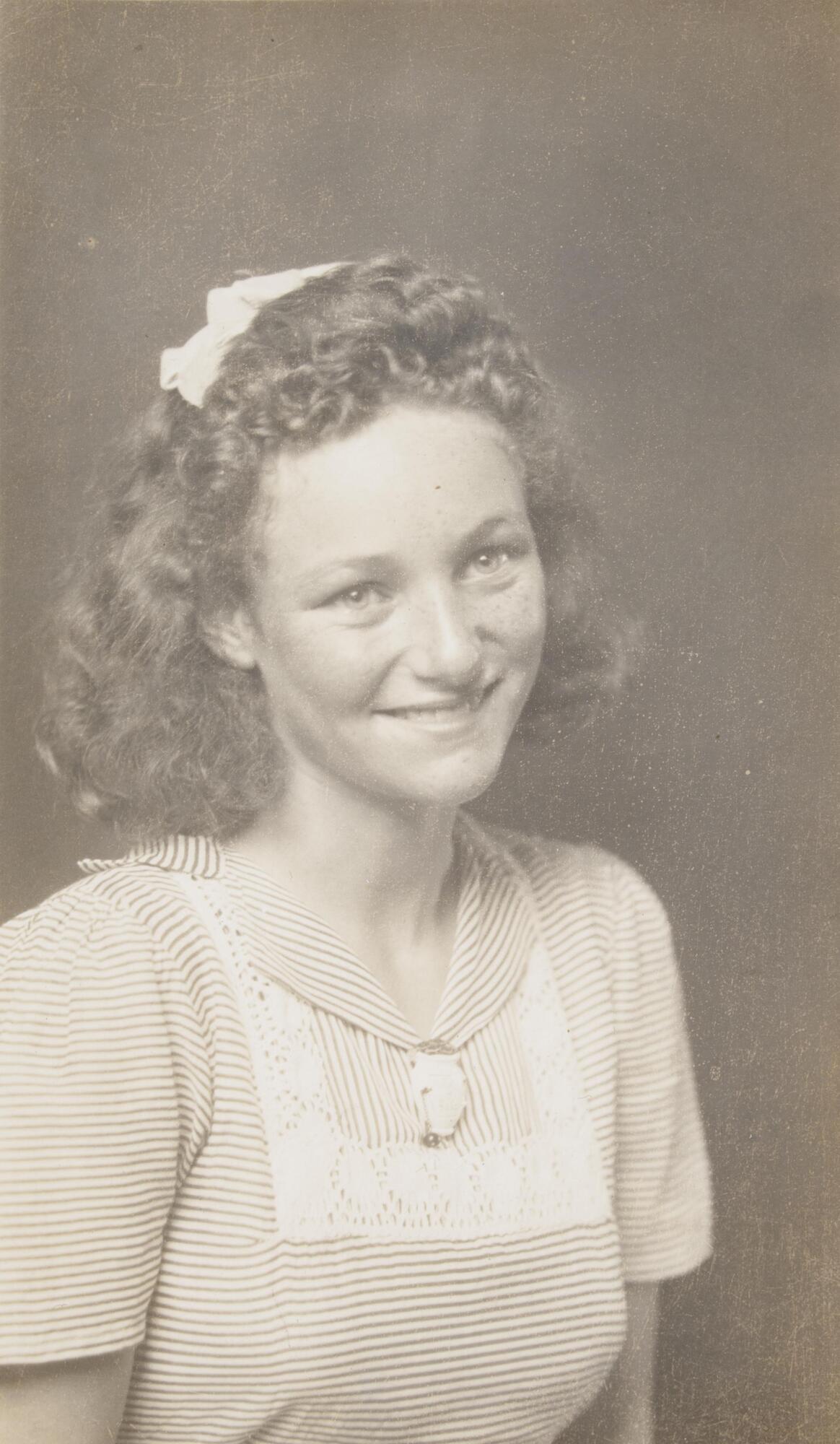 A three-quarter view portrait of a young woman. She wears a striped, collared dress with a lace decoration over the chest, and a ribbon in her curly hair. 