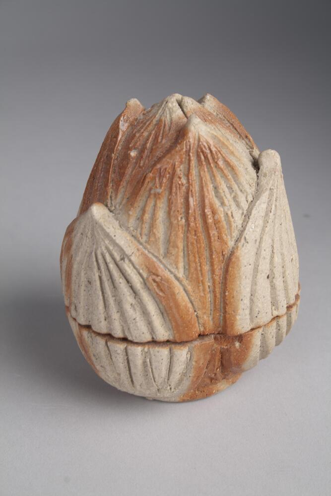 A ceramic incense box in beige and reddish orange color. Shaped like a closed flower bud with smaller leaves covering it.