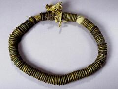 Belt with large brass rings strung on a thick cord. Some of the brass rings have incised grooves while others are smooth. 