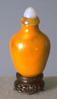 A Baltic amber snuff bottle with with wide shoulders and thins towards the bottom. On the top of the snuff bottle is a moonstone stopper sit in a horn collar.