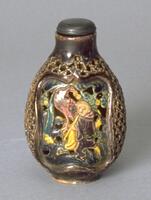 A gold/brown snuff bottle with patterned holes throughout the bottle. In the middle of the snuff bottle is an image of a man playing a flute. At the top is a black snuff bottle.