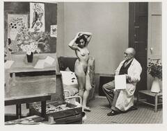 Artist sitting in a studio, studying a female nude model posing in front of him.