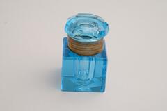 A small, bright blue inkwell. The base is glass and square shaped, while the lid is cut crystal.