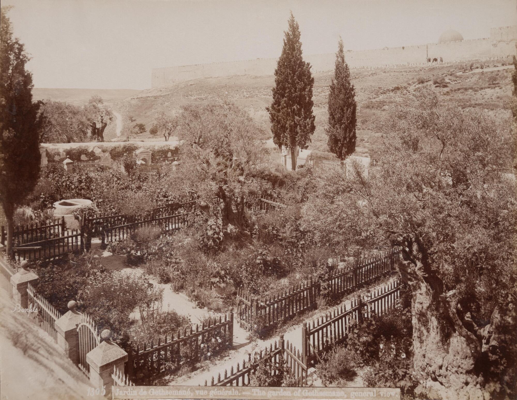 A view down onto a fenced-off garden; a crenellated stone wall and dome are visible in the background. 