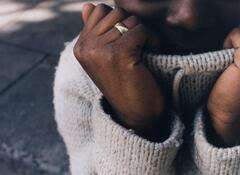 A close-up of a woman's hands on her face, she is wearing a beige sweater and has a gold ring on her finger.