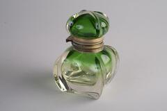 A square glass inkwell.  The stopper is dark green and the color fades down the inkwell.
