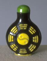Circular black glass snuff bottle with I Ching (Chinese fortune telling) in the surface in yellow. On the top is a green stopper.