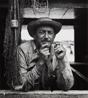 Half-length image of an elderly man in a straw hat holding a cigarette as he looks out toward the viewer. 