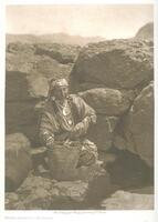A woman kneeling in a rocky landscape. She is near a stream with a vessel for water in her hands. She wears her hair in long braids and a cloth on her forehead.