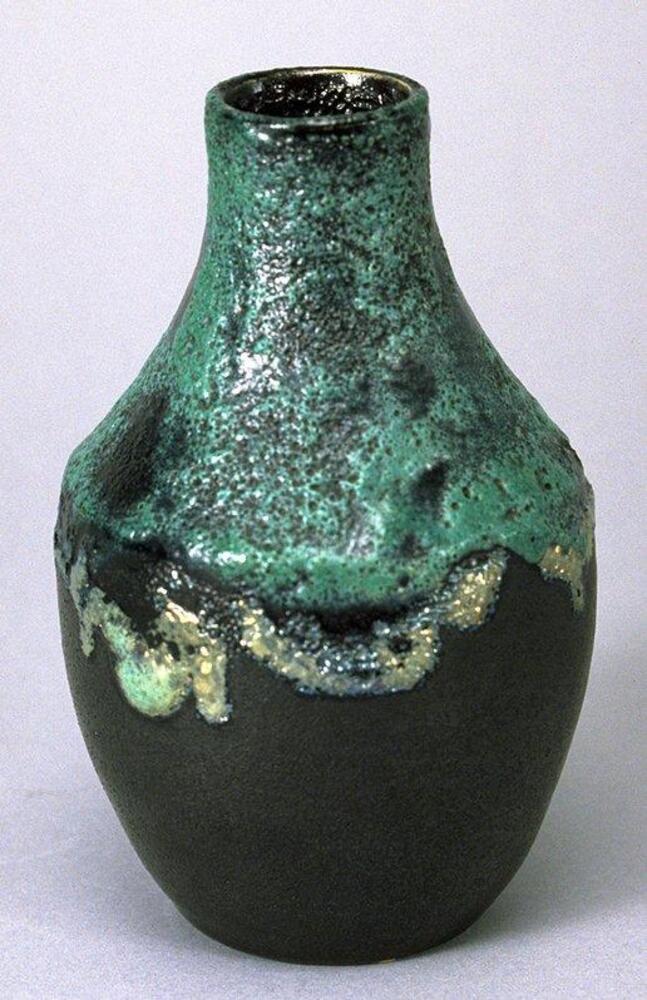 This small vase has a matte black glaze on the lower portion and a thick green glaze with many bubbles in it that extends from the narrow mouth across the shoulder of the vessel.