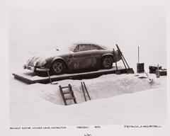 A car under excavation in a snowy scene. There is excavation equipment around the car as well.