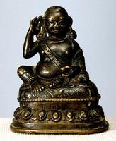 A miniature sculpture of a the Tibetan yogin Milarepa as a rotund figure, seated in lalitasana (the posture of royal ease, with one knee drawn up and the other relaxed) on an antelope skin (the head of the antelope can be discerned just under the figure's left foot, as an incised design). The right hand is raised, cusping the right ear as though to better hear, while the left elbow rests on the left knee, and the right hand holds a nettle-shell bowl. Wrapped around his torso, from his right shoulder to his left knee, is a sash (sometimes referred to as a meditation belt), which allows him to keep his body upright during long hours of meditation. The base, cast in a single piece with the figure, is decorated with beading and a single band of lotus petals.