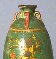 A tall stoneware ovoid bottle on a straight footring with a narrow, short, flaring neck and a direct rim. It has four loop handles connecting the neck to shoulder, incised with floral decoration, and the upper half of the body is covered in green, amber, and yellow polychrome glazes. 