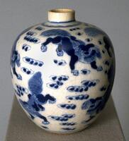 A porcelain globular jar with narrow straight neck and direct rim, on a recessed footring, covered in underglaze cobalt blue paintings of lions among clouds, covered in clear glaze. It is missing the dome cap lid and forms a pair with 1977/2.12.