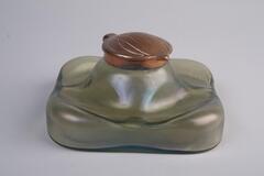 A square, iridescent inkwell. The base is grenn and the lid is gold.