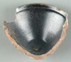 A large, deeply curved, roughly shaped shard covered in black glaze with hare's fur (兔毫盏 <em>tuhao zhan</em>) markings. Broken edges expose a brown ceramic body, on a straight, tall foot ring. 
