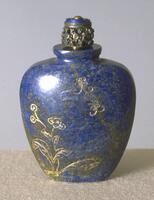 A lapis lazuli snuff bottle that has rounded shoulders and thins towards the base. Carved on the surface of the bottle are flowers and butterflies. On the top of the bottle is a lapis lazuli stopper with holes carved into it.