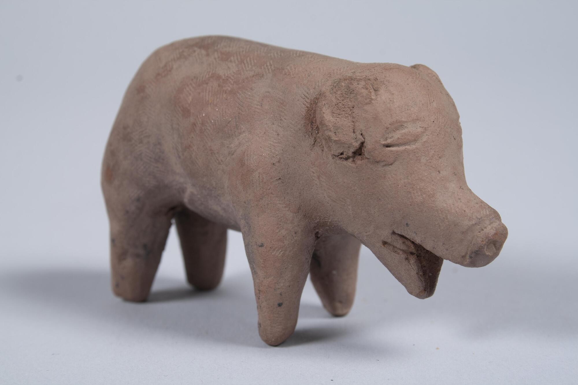 A small figurine of a pig with its mouth open. It is standing with four legs apart and the ears are down.