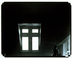 Dark interior lit by window light, featuring a seated nude turned away from the viewer.