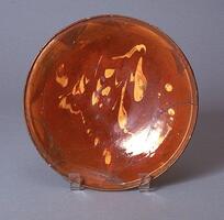 This glazed plate is attributed to the Safavid period in Iran. The interior decoration consists of yellow splashes on a glossy red-brown glaze. 