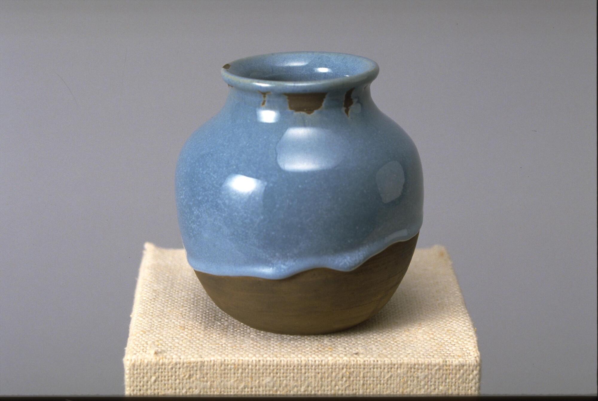 Vessel with rounded body, short neck and wide mouth. Brown clay body with wiped on black slip is covered with a pearlescent thick sky blue glaze dripping down two-thirds of the vessel.